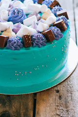 Blue festive cake with merengue and chocolate cubes on a wooden background