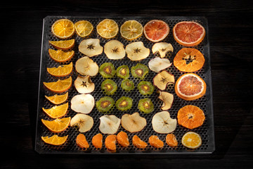 Variedad de frutas deshidratadas en bandeja metálica sobre un fondo negro.