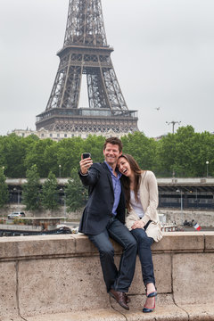 A Laughing Young Couple Take a Photo on a Bridge in Paris, with the Eiffel Tower behind Them