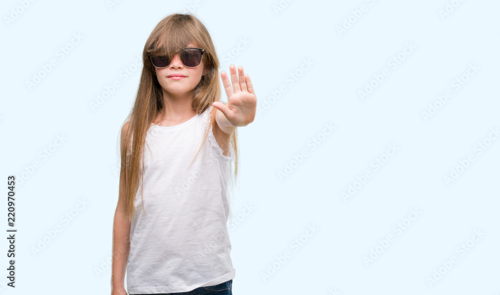 Sticker Young blonde toddler wearing sunglasses with open hand doing stop sign with serious and confident expression, defense gesture