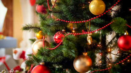 Closeup image of red and golden baubles hanging on fir tree decorated for Christmas