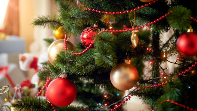 Closeup image of colorful lights and baubles hanging on Christmas tree at living room