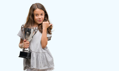 Brunette hispanic girl holding a trophy pointing and showing with thumb up to the side with happy...