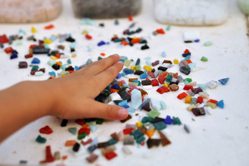 Pieces of colored glass mosaic in the child's hand on the table. Creativity and learning.