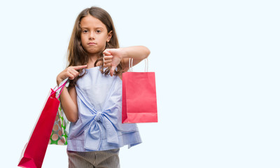 Brunette hispanic girl holding shopping bags with angry face, negative sign showing dislike with thumbs down, rejection concept