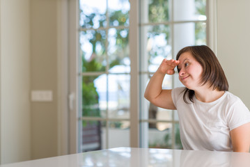 Down syndrome woman at home very happy and smiling looking far away with hand over head. Searching concept.