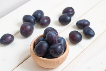 Ripe juicy plums in wooden bowl on rustic wooden table