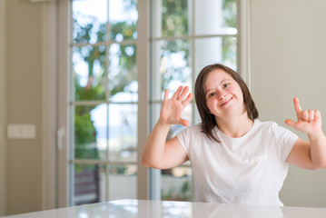 Down syndrome woman at home showing and pointing up with fingers number seven while smiling confident and happy.