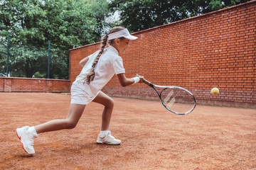 Child playing tennis on outdoor clay court. Full length shot of a tanned little girl on tennis...