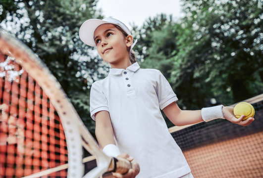 Active exercise for kids on tennis court. Portrait of sporty little girl on tennis court. Summer activities for children.Child girl ready to serve tennis ball outdoors.