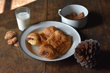 Plato y taza vintage con bollería , vaso de leche y piña de pino de adorno