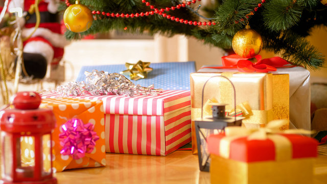 Closeup image of colorful gift boxes and lanterns under Christmas tree at morning