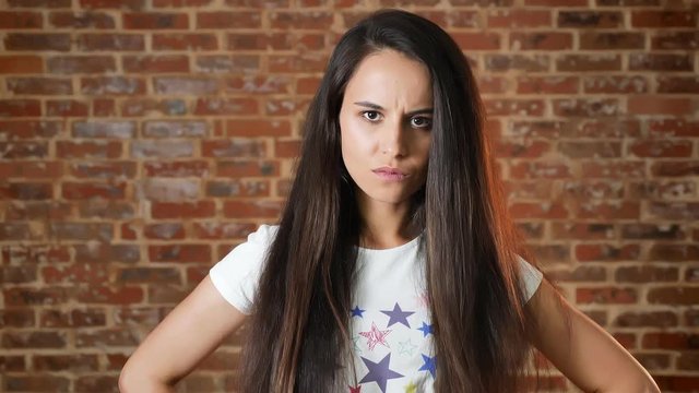 Young angry girl clenching her fist and looking into the camera, threatening, brick wall in the background, portrait