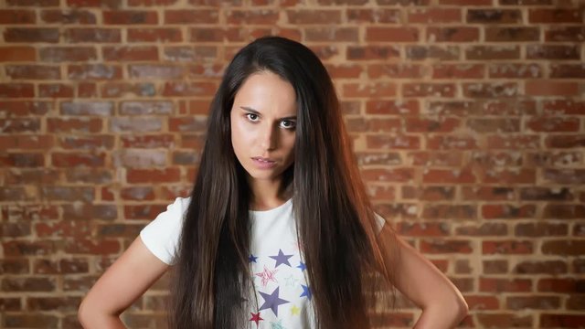 Young girl looking at the camera, haughty, brick wall in the background, portrait