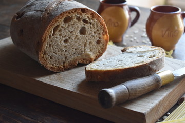 Pan de galicia sobre tabla de madera, vasos de vino de barro