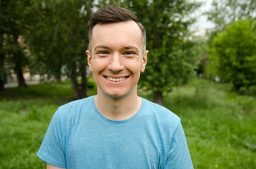 Young smiling guy on a green grass and trees background.
