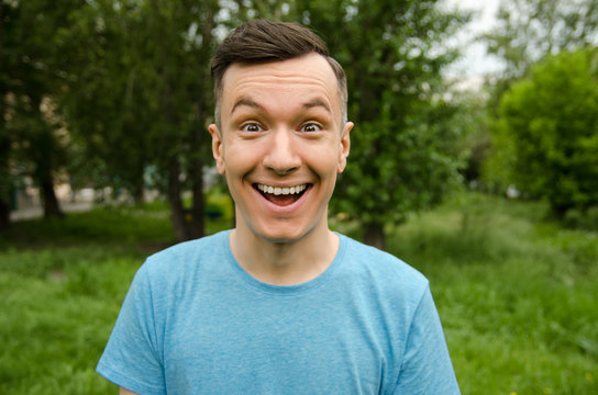 Young smiling joyful guy on a green grass and trees background.