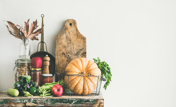 Autumn Seasonal Food Ingredients, Kitchen Utensils. Vegetables, Pumpkin, Apples, Canned Food, Fallen Leaves Over Rustic Wooden Chest Of Cupboard, Copy Space. Thanksgiving Dinner Preparation