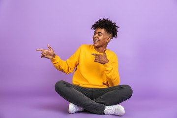 Portrait of stylish african american guy smiling and pointing fingers aside at copyspace while...