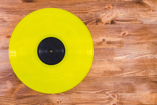 Yellow color vinyl record on brown wooden background
