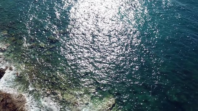 Aerial view of crystal clear waves at a rocky coast with clear blue water - camera tilt and pan