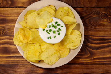 Crispy potato chips with green onion and sour cream on wooden table. Top view