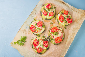 Healthy, nutritious zucchini small round pizza with pepperoni, tomatoes, cheese and parsley on parchment paper on light blue background.
