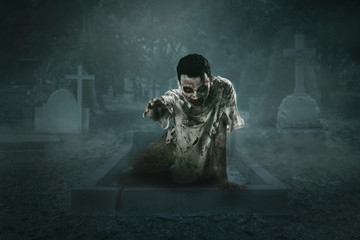 Horrible male zombie crawls out of the grave