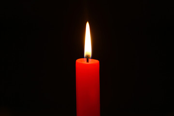 small paraffin flaming red candle with big flame against the dark background.