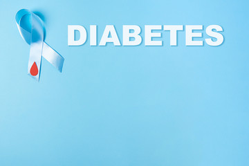 inscription diabetes and blue ribbon awareness with red blood drop on a blue background, world diabetes day