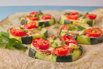 Healthy, nutritious zucchini small round pizza with pepperoni, tomatoes, cheese and parsley on parchment paper on light blue background.
