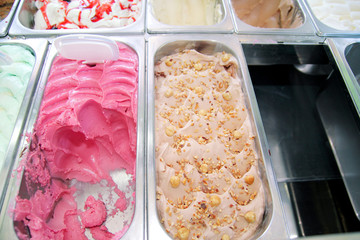 Bar with many flavors of delicious ice cream for sale. Fridge with creamy of hazelnut flavors, raspberry and cherry in serving steel container. Sweet dessert with decorating elements. Pastry shop.