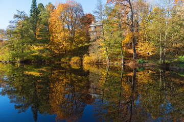 Obraz premium Trees in autumn colors on a lake with a house on a hill reflected in water