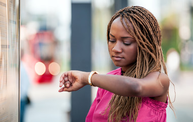 Young African woman checking plan and waiting at city bus stop