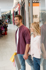  smiling young couple with paper bags walking out from store at shopping mall