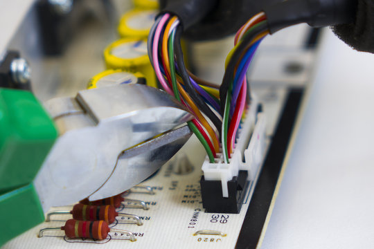 Dismantling electronic bomb, tongs cut the red wire into a bundle of colored wires on the background of the motherboard or electronic chip