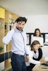 Handsome businessman using mobile phone in the office while other business people sitting in background