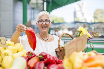 Good-looking senior woman wearing glasses buys pepper on market