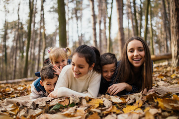 Group of children playing in autumn park. They lying on leafs, smiling and looking at camera.