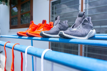 Two pairs of running shoes, red and grey, putted on the cloths hanger to dry in the sun after washing inside the back of the house.