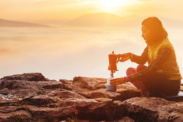 A woman traveler boils a geyser coffee machine and drinks a hot drink from the mug, admiring the...