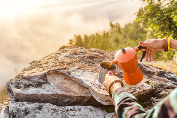 coffeepot and coffee in cup near camping site at foggy mountains background