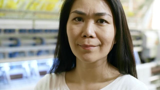Tilt up of attractive middle-aged asian woman posing at camera with industrial textile machine in background