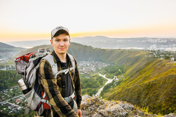 Young traveler stays on a top on a hills and village background.