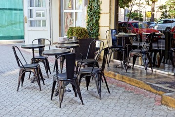 Fototapeta na wymiar black table and chairs on the sidewalk in the summer restaurant at the glass showcase