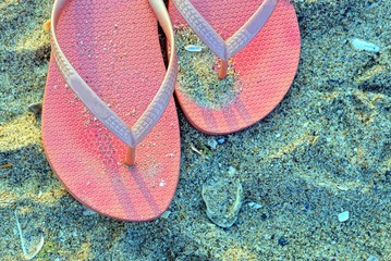 two red dirty plastic slippers in the sand on the beach