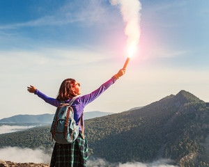 A woman in the wild mountains gives a distress signal SOS using Falsch feuer torch from which comes...