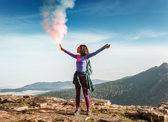 A woman in the wild mountains gives a distress signal SOS using Falsch feuer torch from which comes...