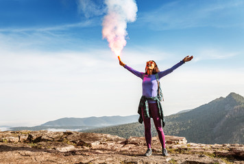 A woman in the wild mountains gives a distress signal SOS using Falsch feuer torch from which comes...