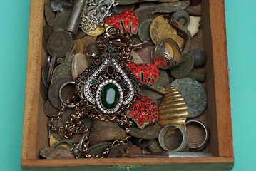 An open wooden box with old jewels on a green background